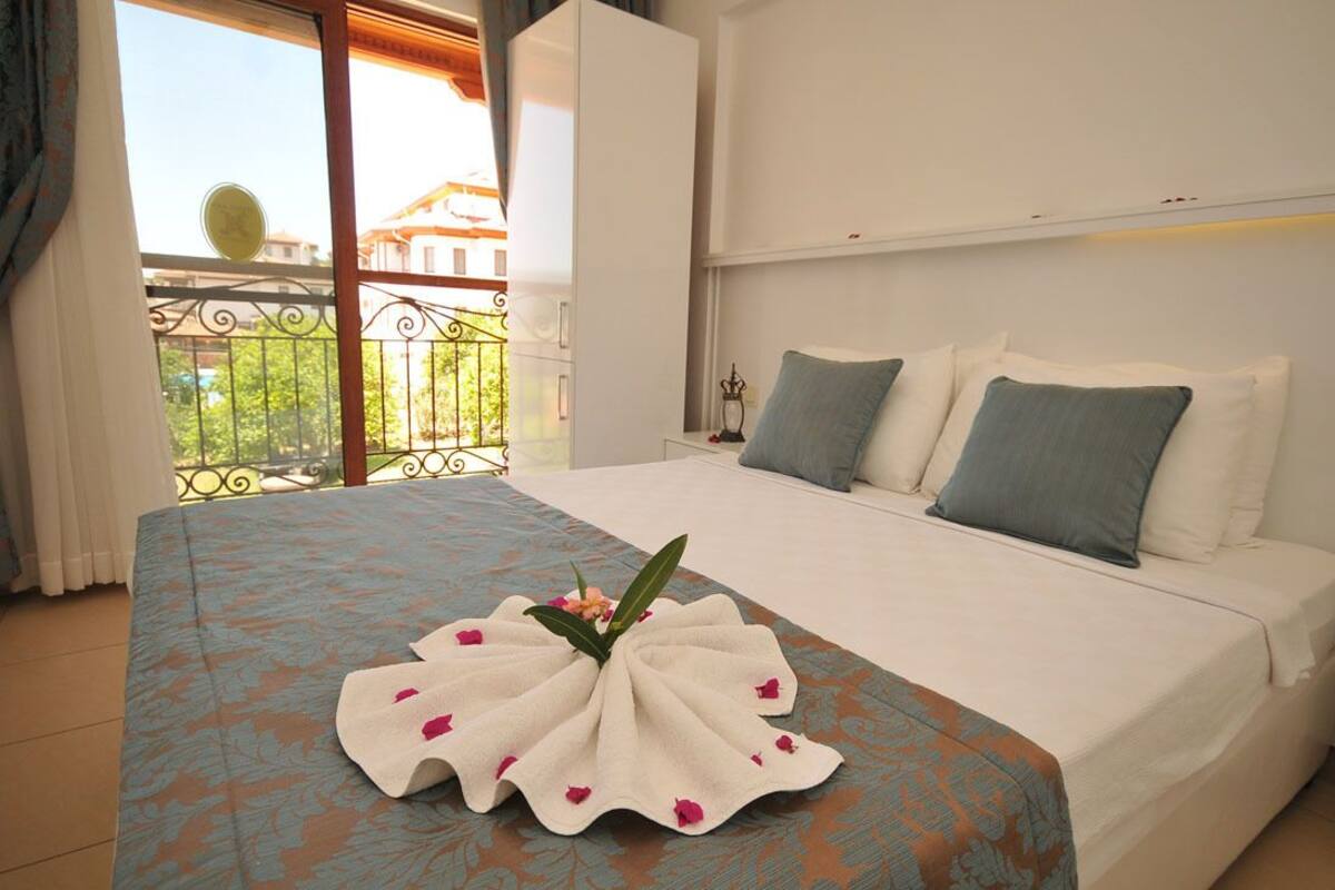 Habitación de hotel con cama, balcón con vistas y una toalla decorativa sobre la cama.