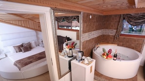 Una habitación con sofá blanco, un espejo grande, una bañera blanca con flores y una mesita con una botella y vasos.