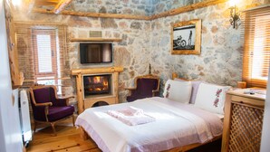A cozy room with a stone wall, a fireplace, a bed, a chair, and a television. - Mogla Tashan Boutique Otel (Mugla)