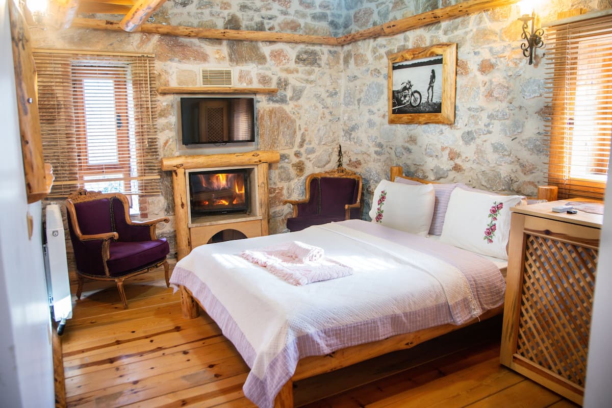 A cozy room with a stone wall, a fireplace, a bed, a chair, and a television.