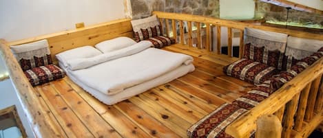 Una cama de madera con ropa de cama blanca y almohadas estampadas en una habitación rústica con paredes de piedra y vigas de madera.
