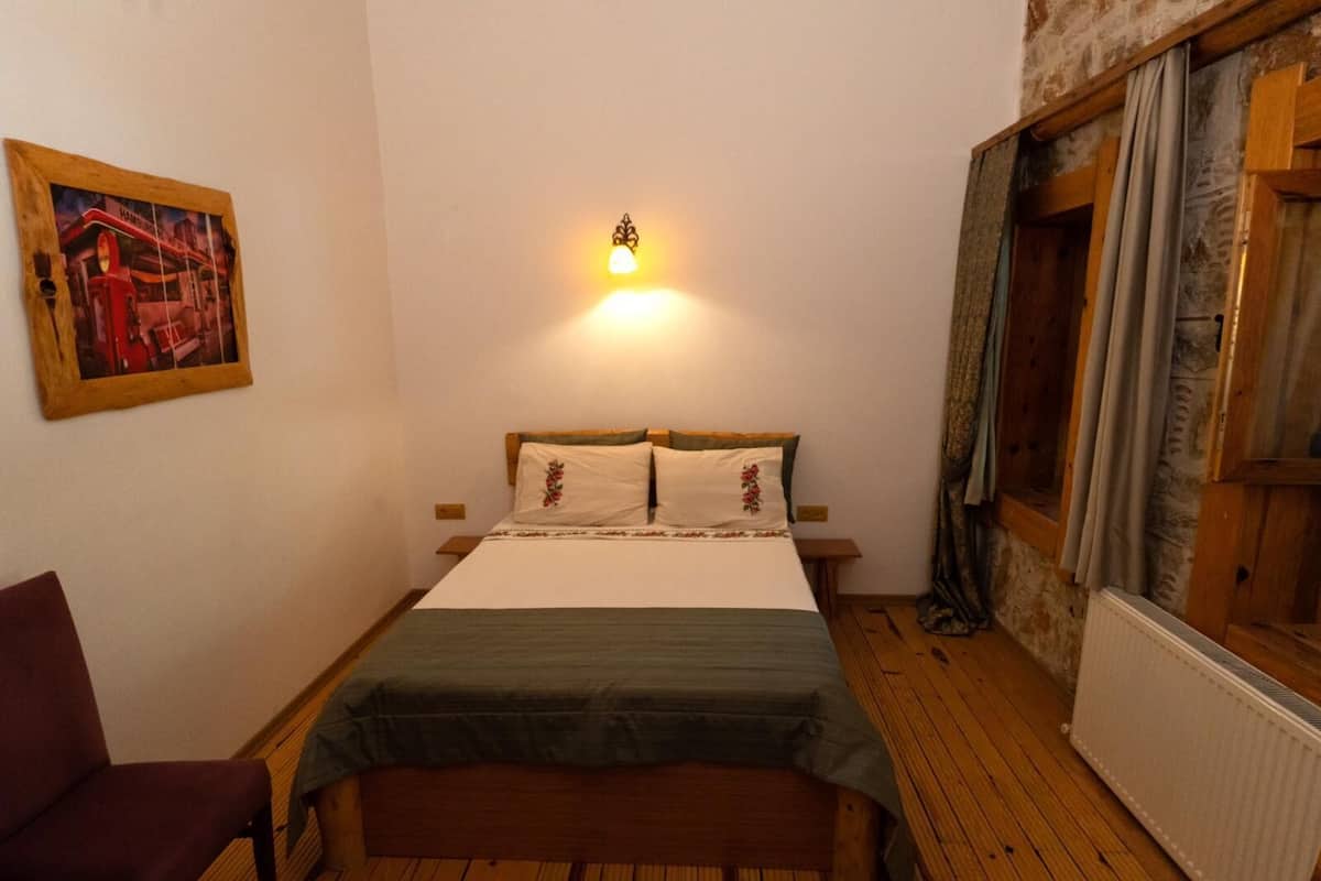 A small, cozy bedroom with a single bed, a nightstand, a chair, and a wall-mounted light.