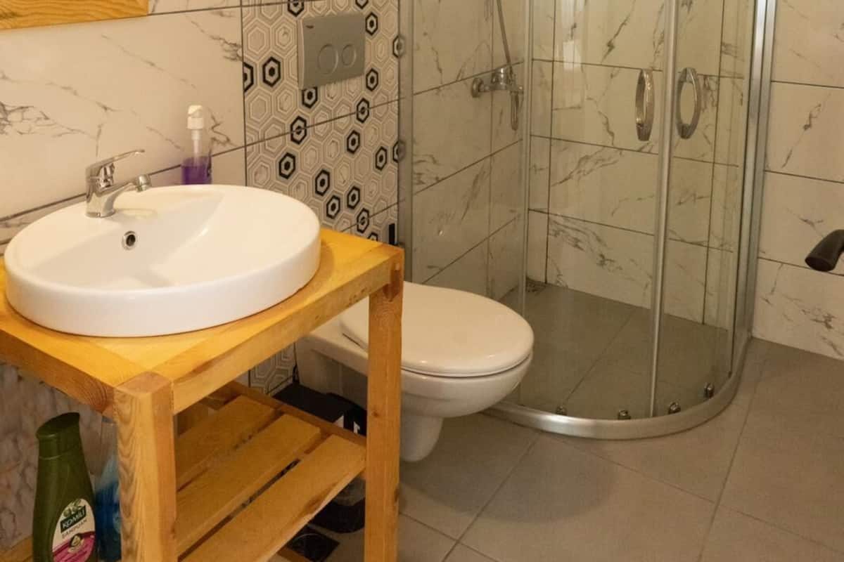 A bathroom with a white sink, wooden vanity, a toilet, and a glass shower enclosure.