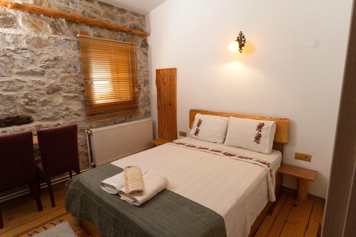 A bedroom with a stone wall, wooden headboard, and a bed with floral pillows.