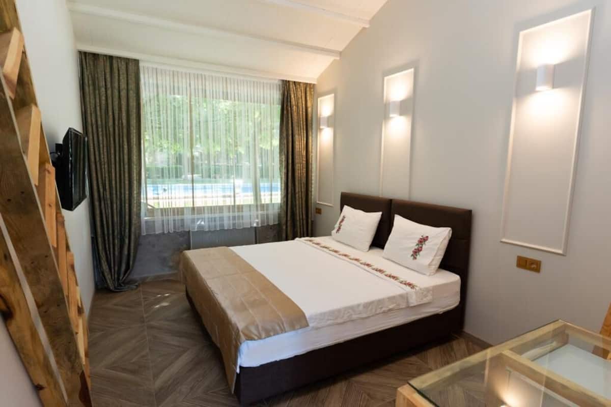 A hotel room with a large bed, a glass coffee table, a TV, and a view of the outdoors through the window.