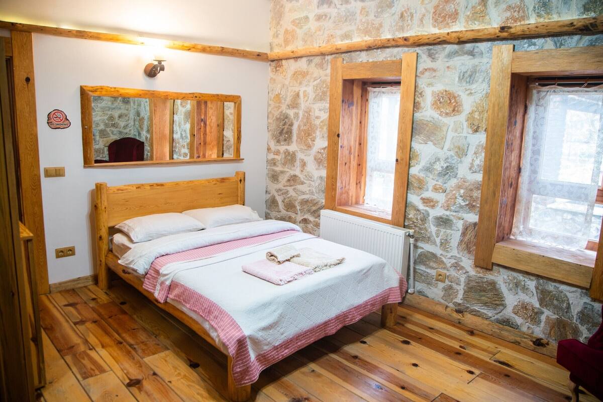A bedroom with a wooden bed, stone walls, and a window with a view.