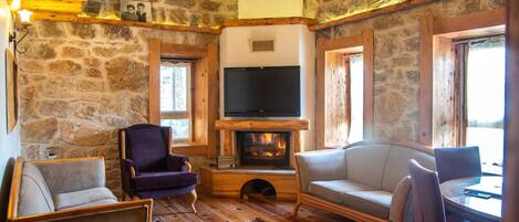 Una habitación acogedora con paredes de piedra, chimenea, televisión y asientos cómodos.