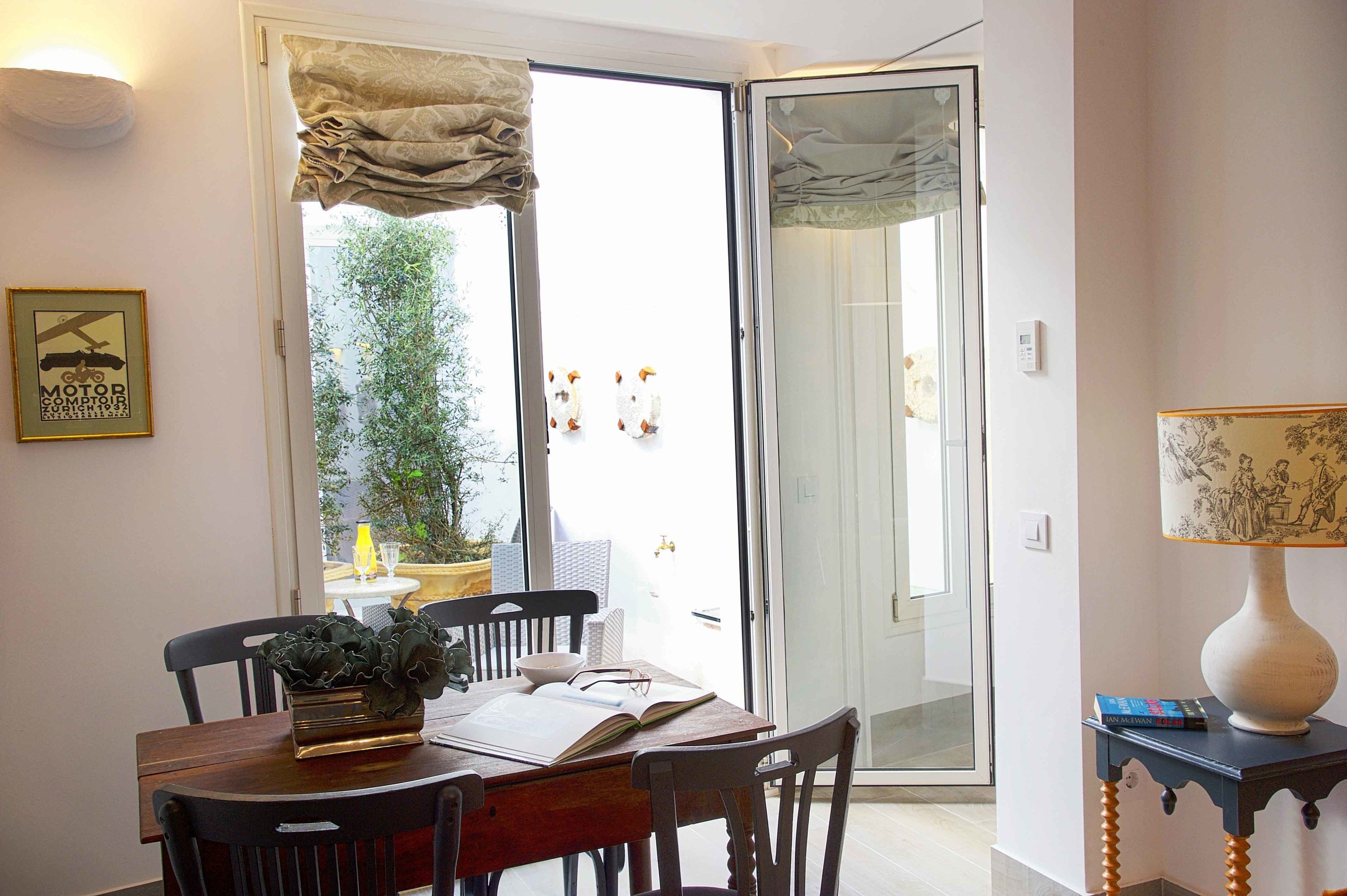 A dining area with a table, chairs, and a book. There is a door leading to an outdoor area with a potted plant.