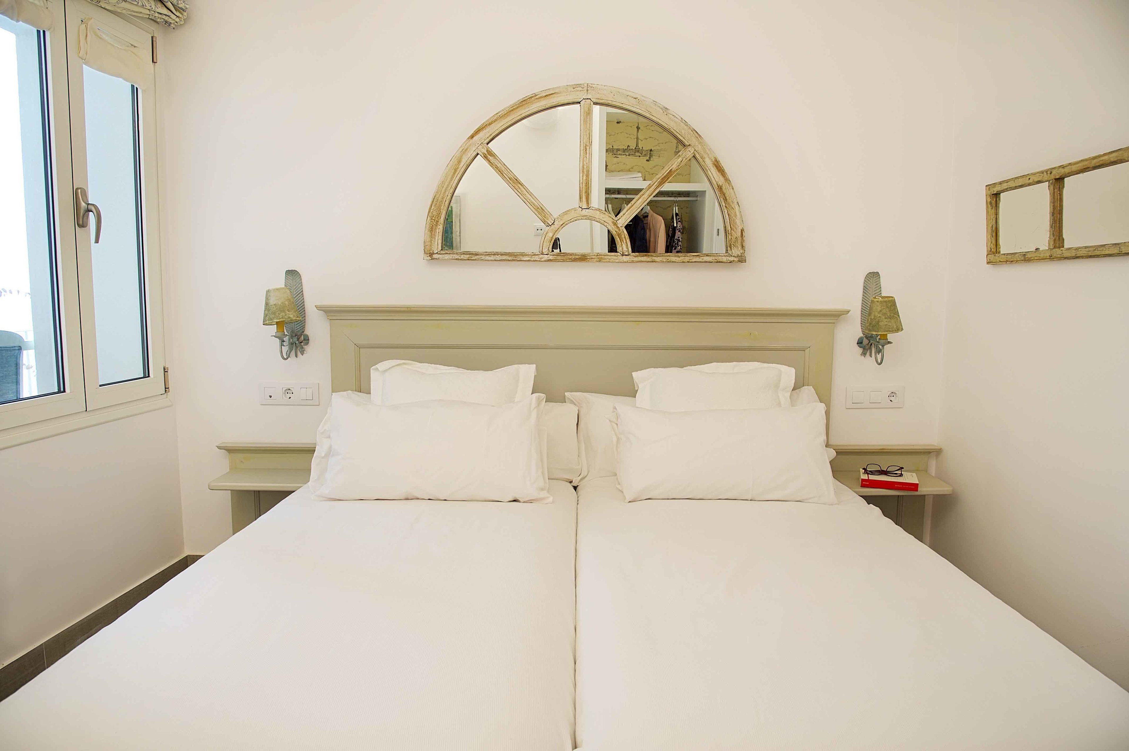 A double bed with white bedding, a mirror above it, and two bedside tables with lamps.