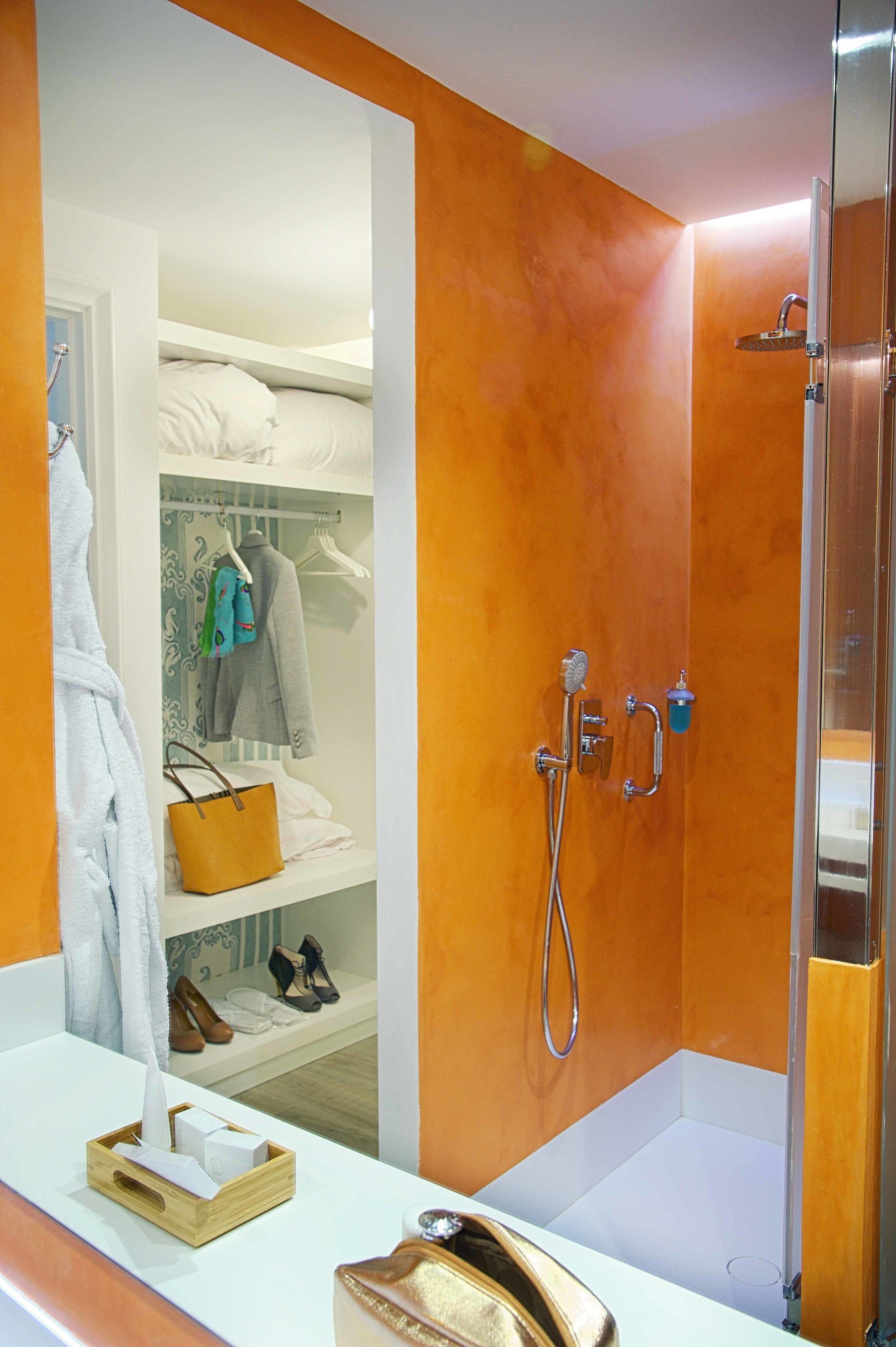 Un baño con ducha, tocador con espejo y armario con ropa y zapatos colgados.