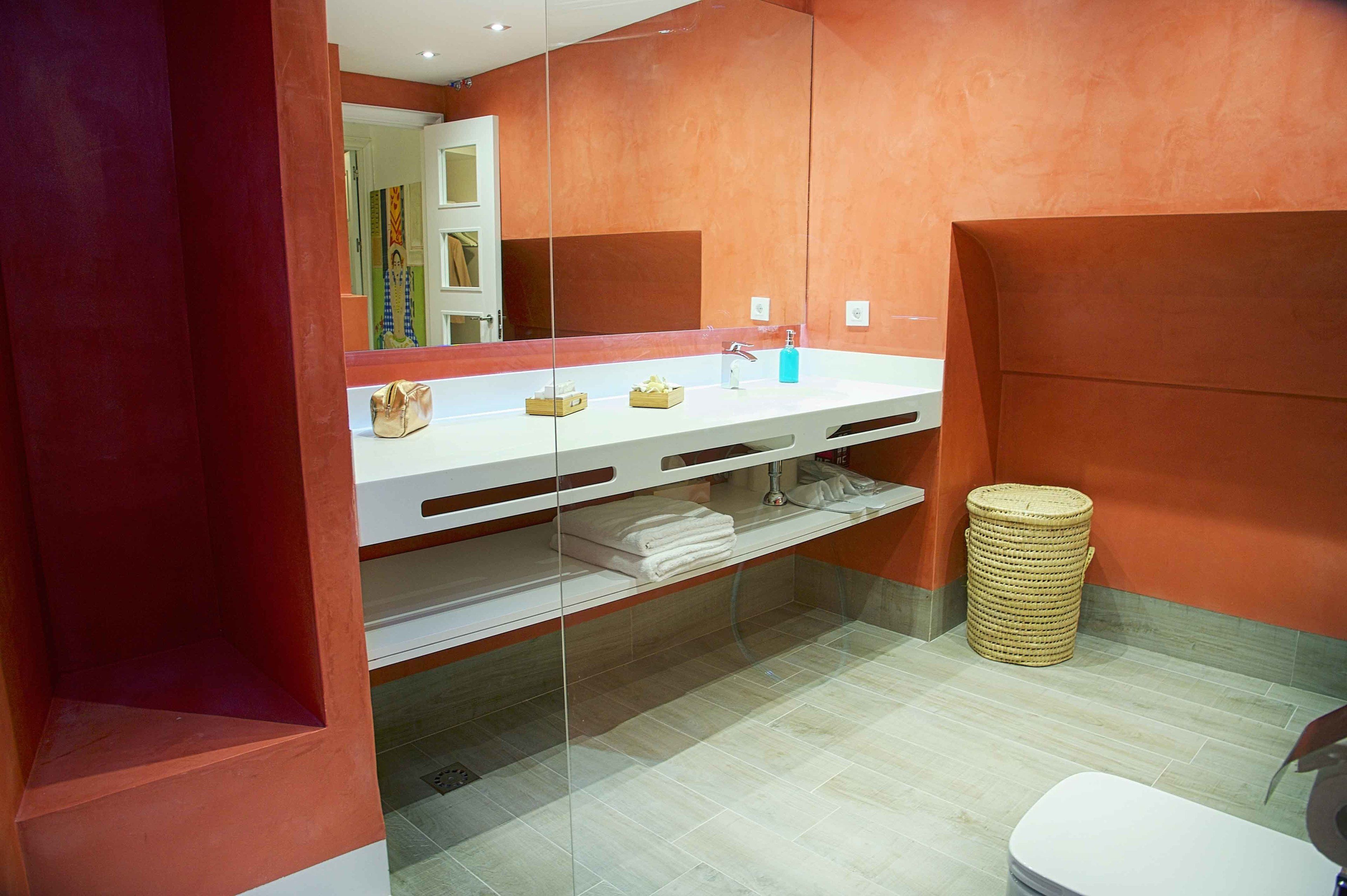 A modern bathroom with a large mirror, white countertop, and a wicker waste basket.