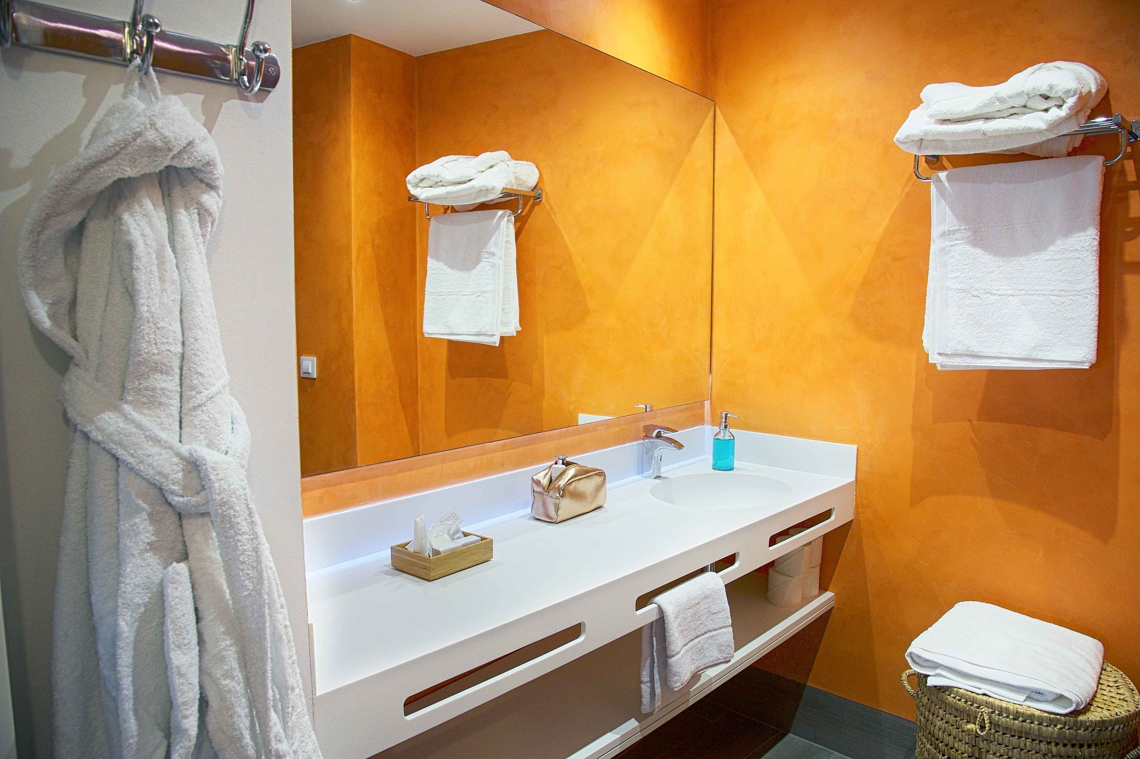 A bathroom with a white vanity, a large mirror, and two towels hanging on the wall.
