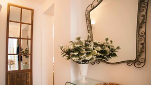 A hallway with a wooden door, a glass console table with a vase of flowers, and a decorative mirror.