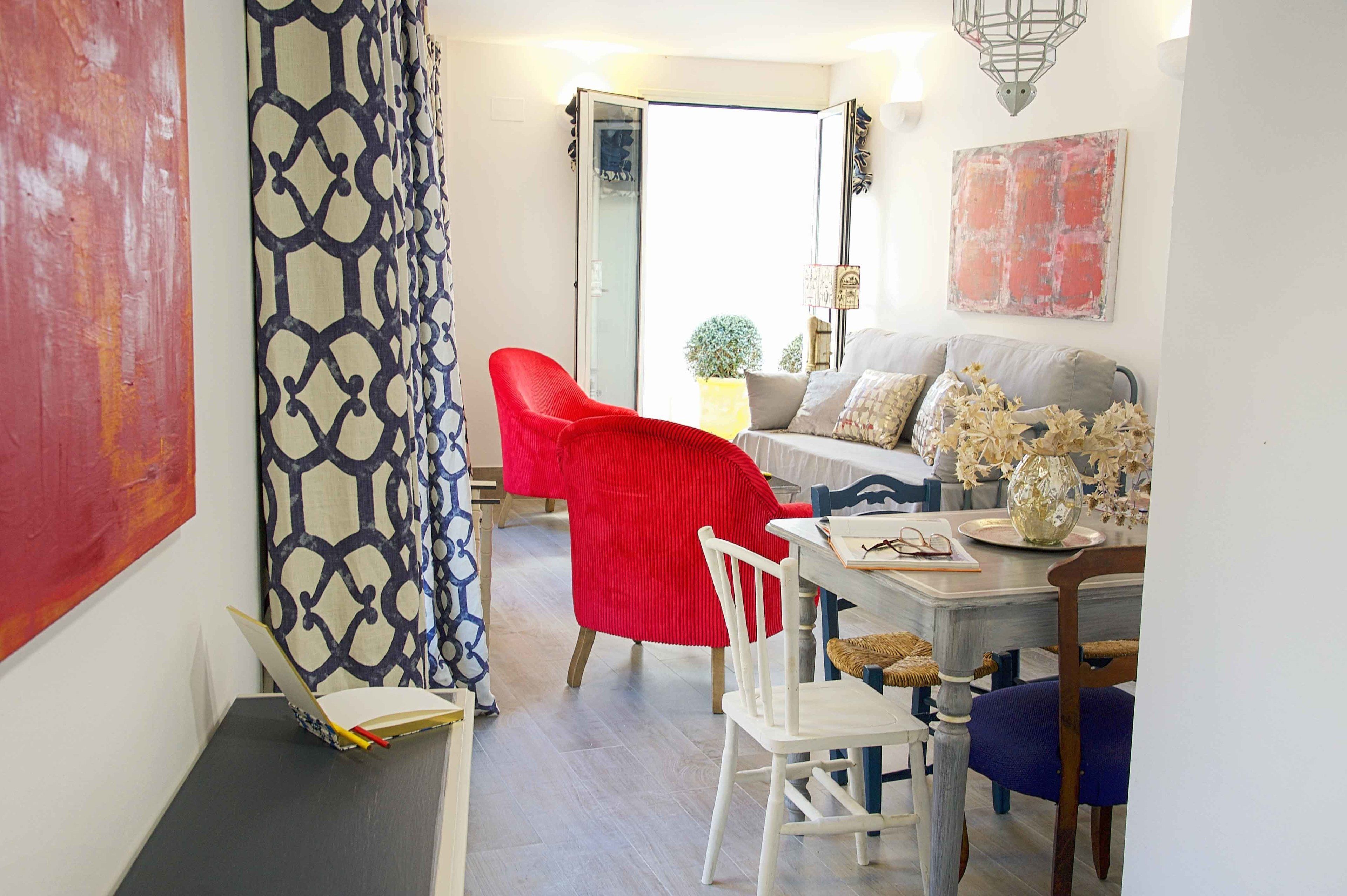 A dining area with a red chair, white chairs, a table with a vase of flowers, and a sofa.