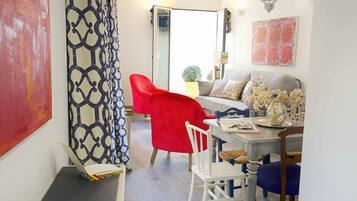 A dining area with a red chair, white chairs, a table with a vase of flowers, and a sofa.