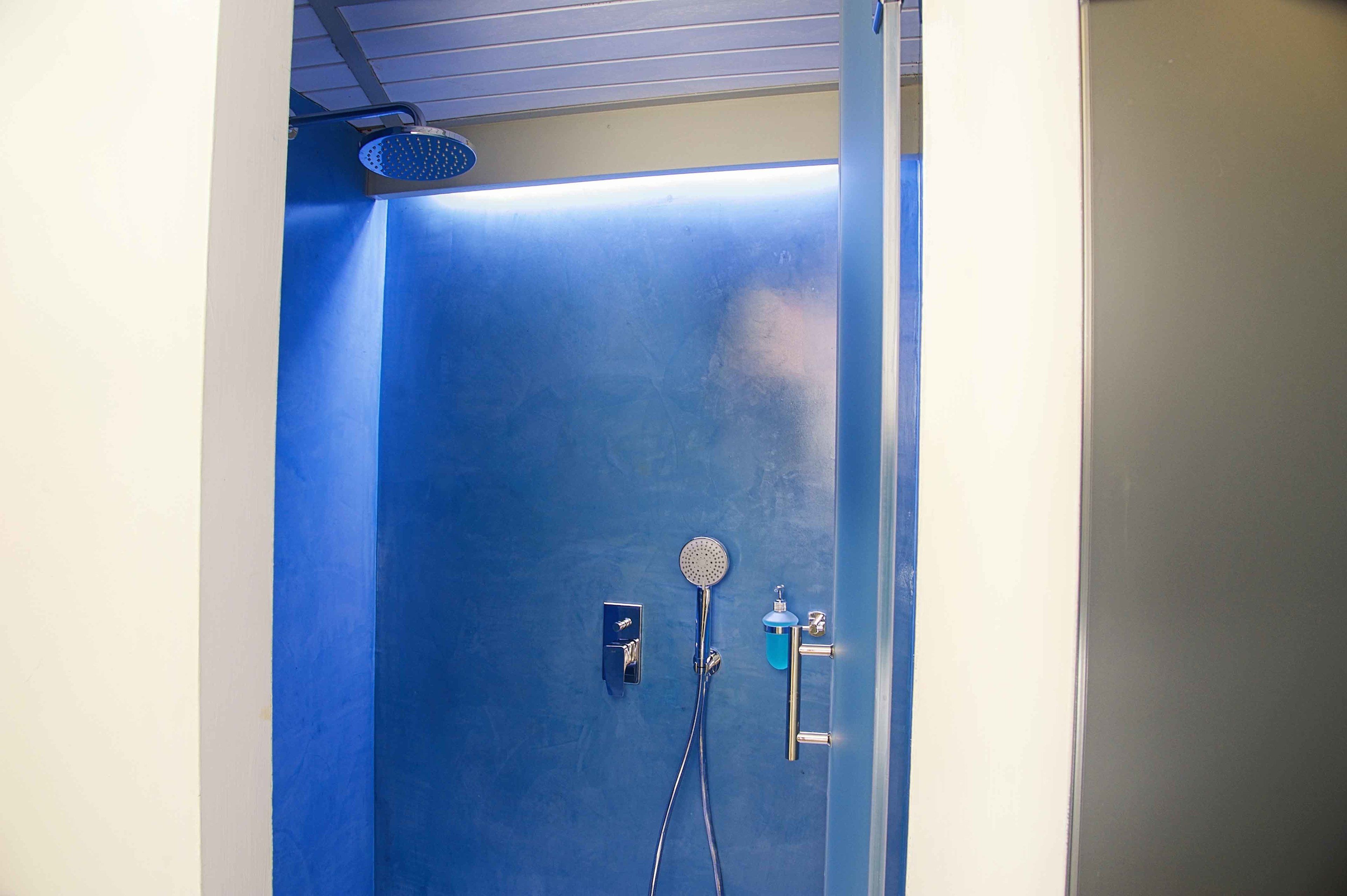 A bathroom with a blue shower enclosure, a handheld showerhead, and a wall-mounted faucet.