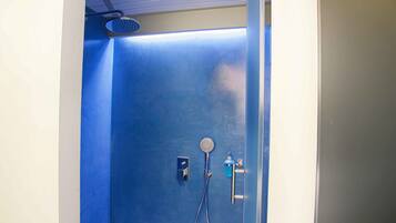 A bathroom with a blue shower enclosure, a handheld showerhead, and a wall-mounted faucet.