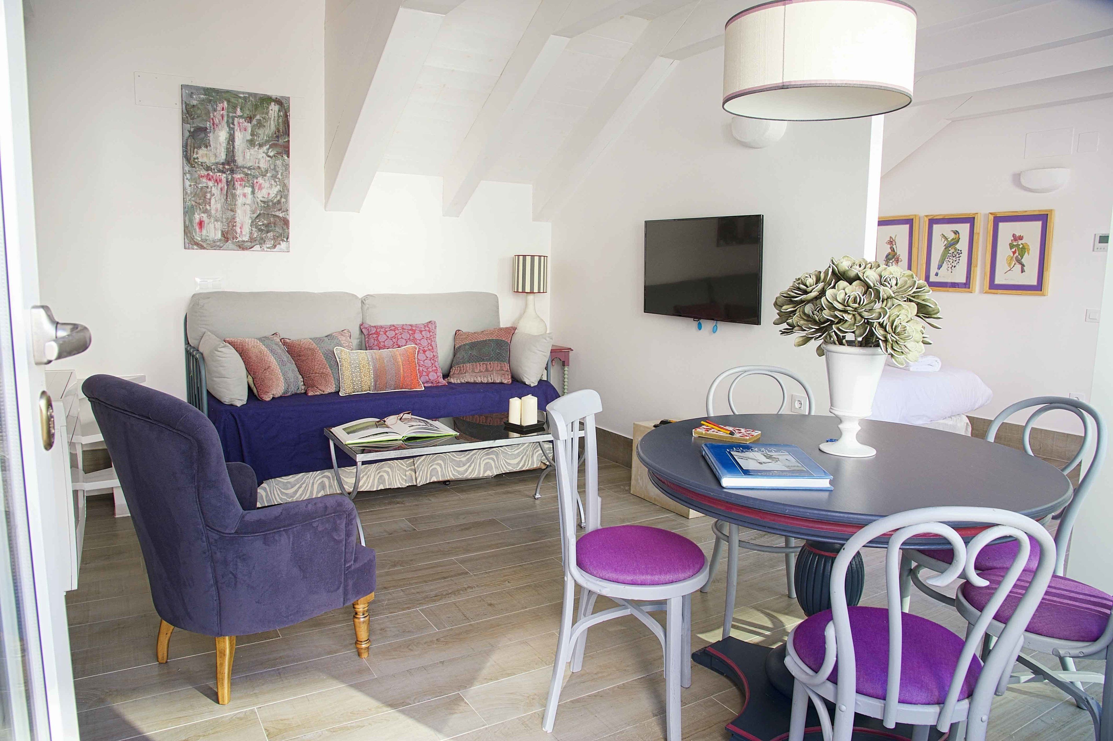 Ein modernes Wohnzimmer mit einer Couch, einem Esstisch mit Stühlen, einem Fernseher und einer Decke mit Dachfenstern.