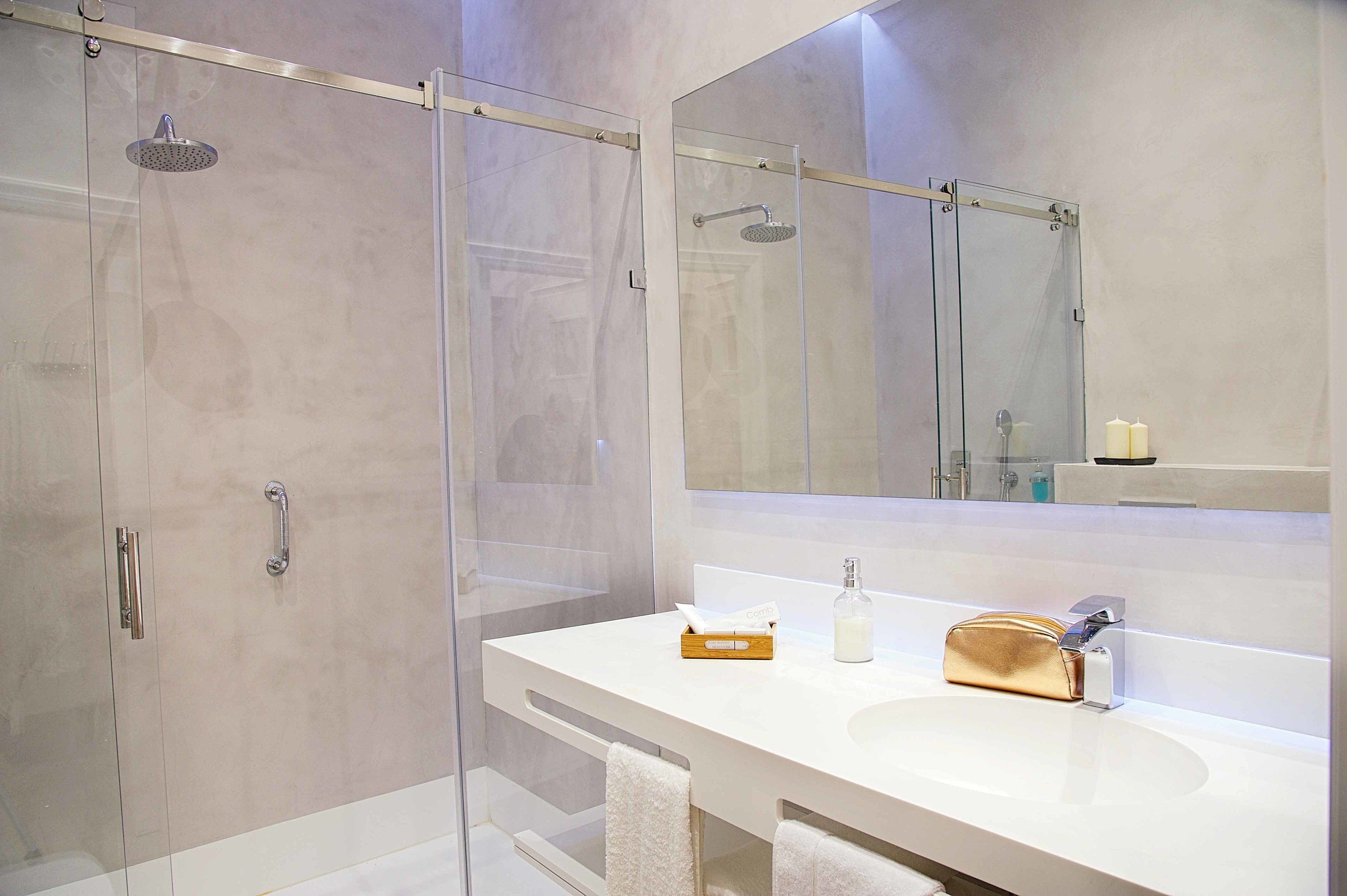 Ein modernes Badezimmer mit einer Glaskabine zur Dusche, einem weißen Waschbecken und einem großen Spiegel.