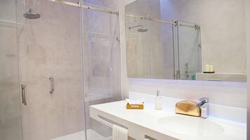 Ein modernes Badezimmer mit einer Glaskabine zur Dusche, einem weißen Waschbecken und einem großen Spiegel.