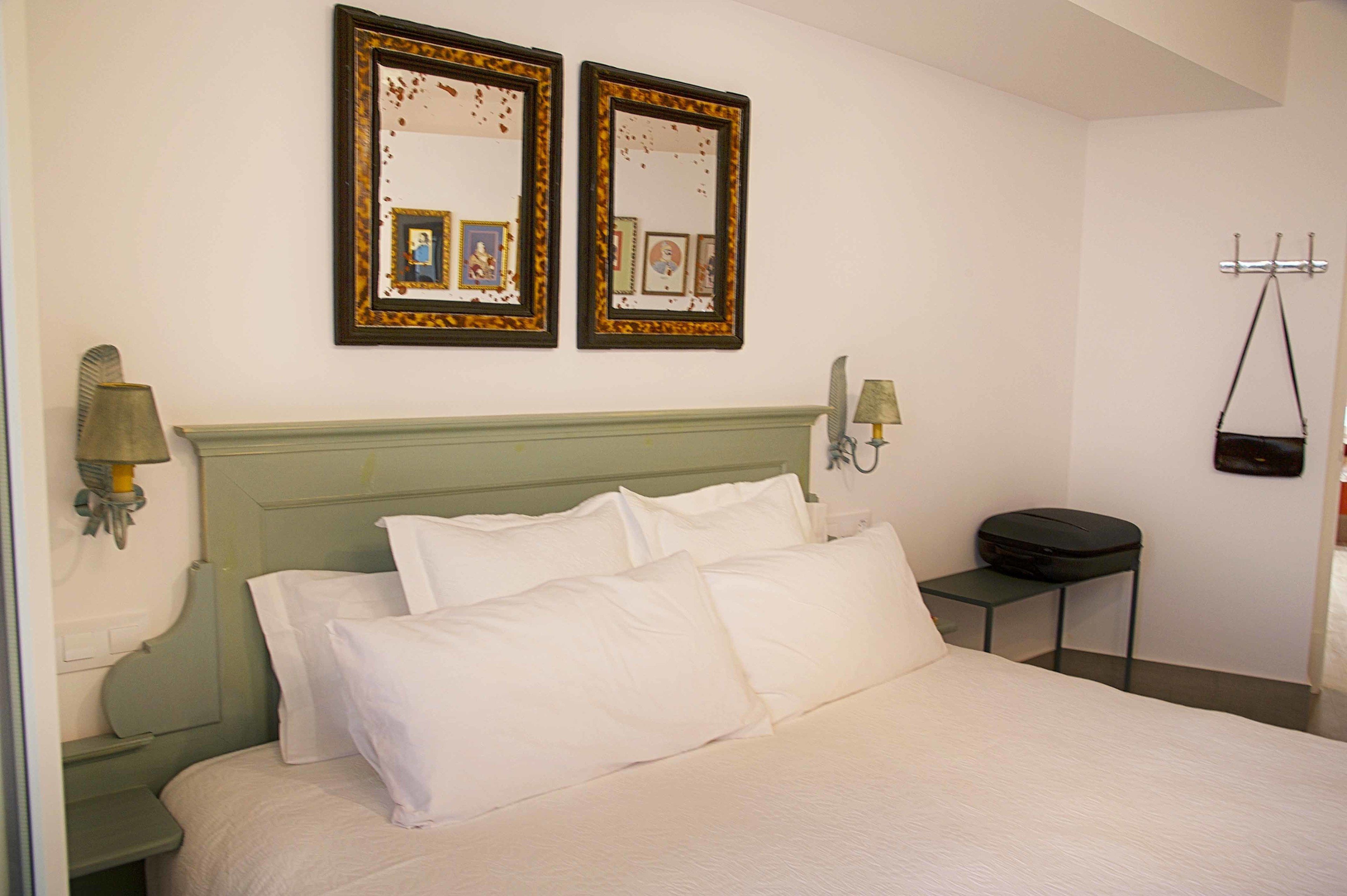 A neatly made bed with white linens, a green headboard, and two framed pictures on the wall above.