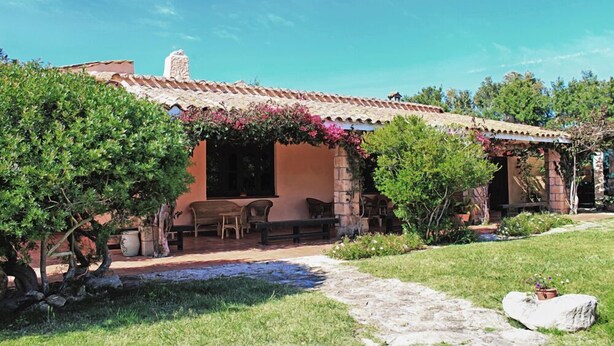 Una casa rústica con techo de tejas, chimenea de piedra y un jardín con sendero.