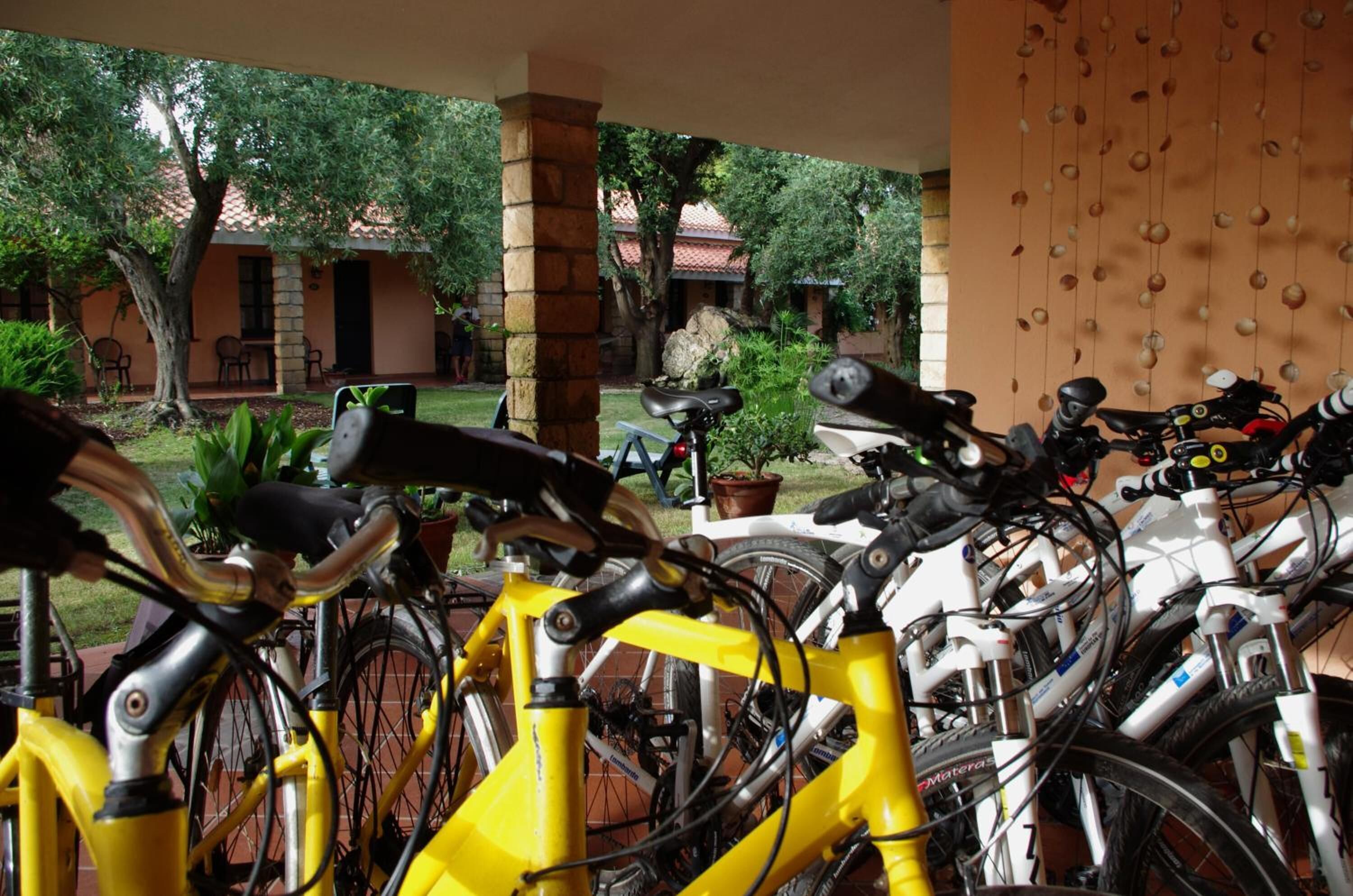 A covered outdoor area with bicycles parked, a stone pillar, and a view of a building with a tiled roof.
