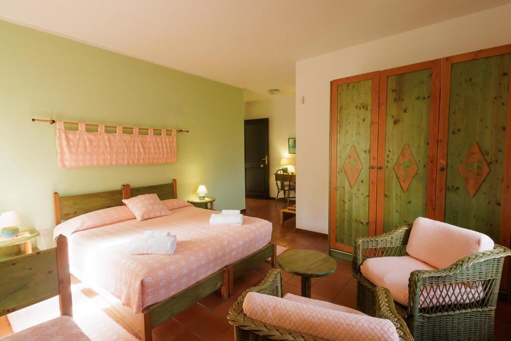 A bedroom with two beds, a green wall, a wooden wardrobe, wicker furniture, and a small table.