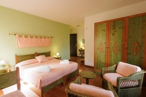 Un dormitorio con dos camas, una pared verde, un armario de madera, muebles de mimbre y una mesita.