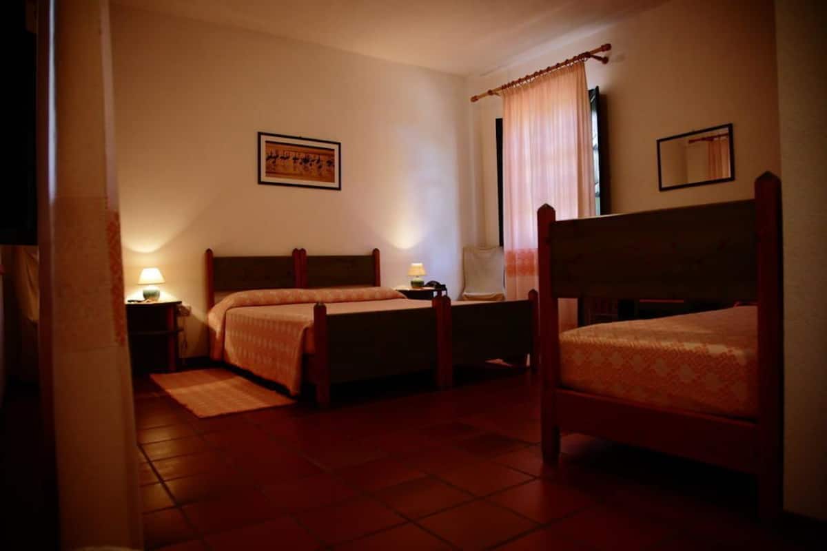 A room with two wooden beds, a small table, a lamp, and a window with curtains.