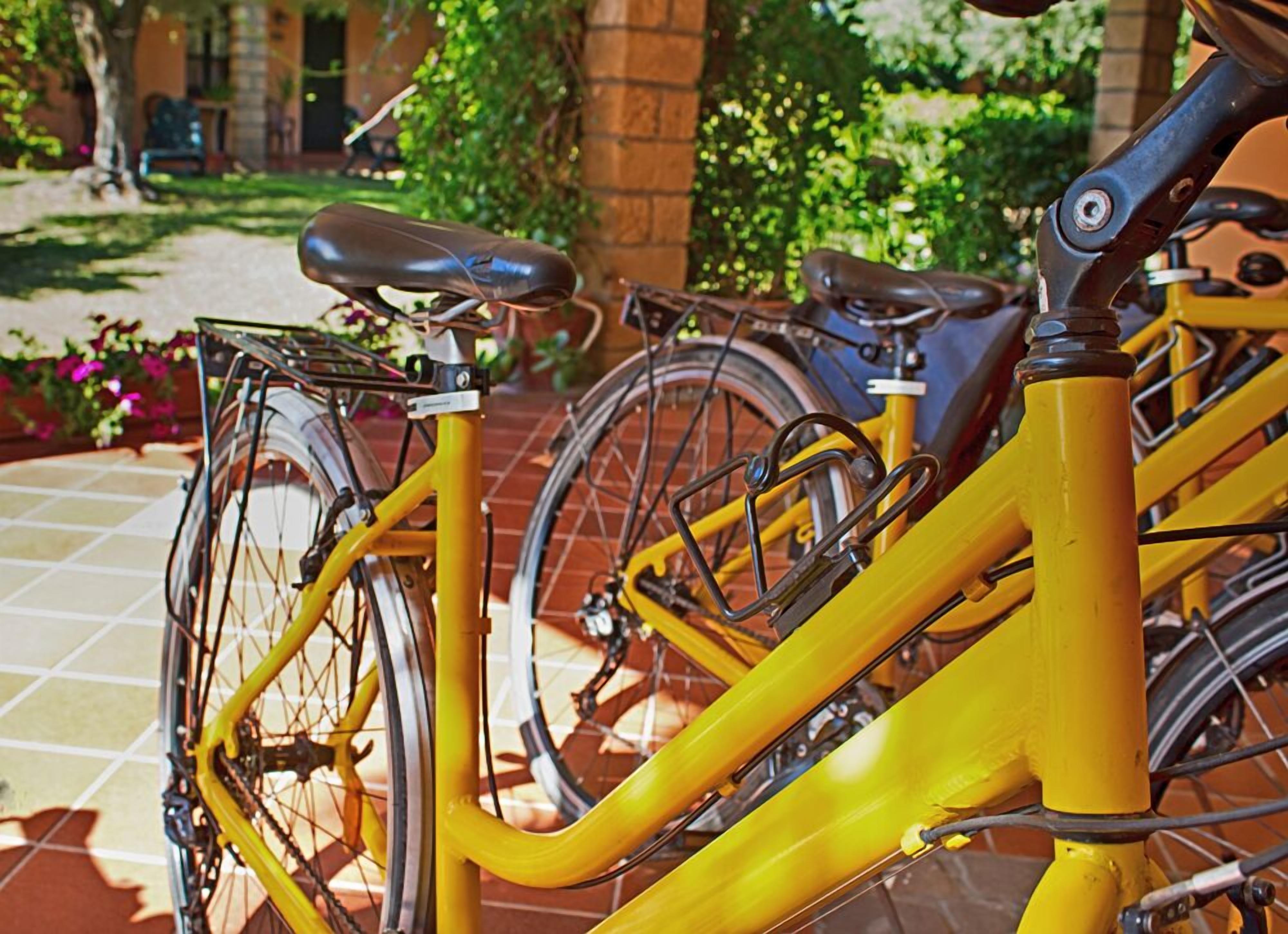 Un vélo jaune est garé sur une terrasse carrelée, avec un mur de briques et de la verdure en arrière-plan.
