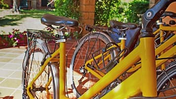 Un vélo jaune est garé sur une terrasse carrelée, avec un mur de briques et de la verdure en arrière-plan.