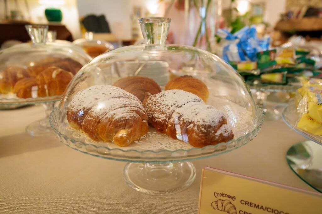 A display of pastries under glass domes, with a sign indicating 'Croissants' and 'Crema/Cioccio'.
