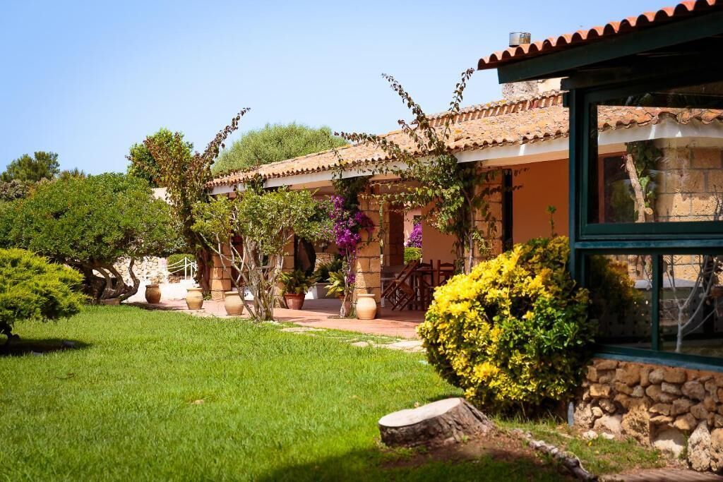 Una casa tradicional con tejado de tejas, muros de piedra y un jardín bien cuidado con diversas plantas y césped.