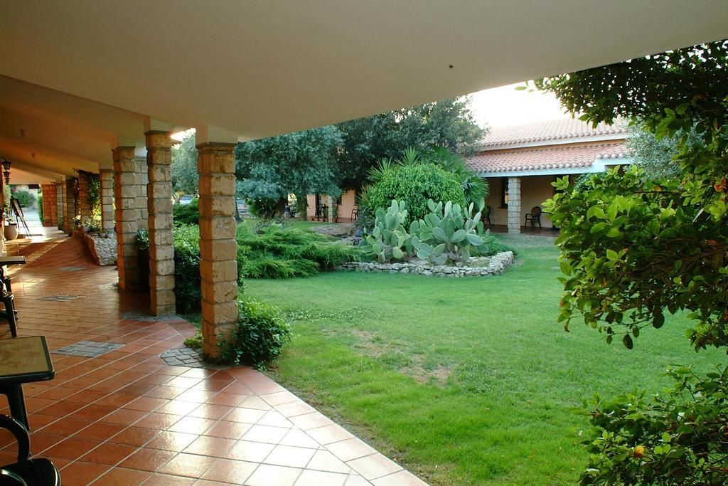 Un cortile con un patio piastrellato, colonne in pietra e un prato curato con diverse piante.