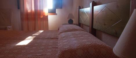 Un dormitorio con una colcha estampada, un cabecero de madera, una mesita de noche con una lámpara y una ventana con cortinas.