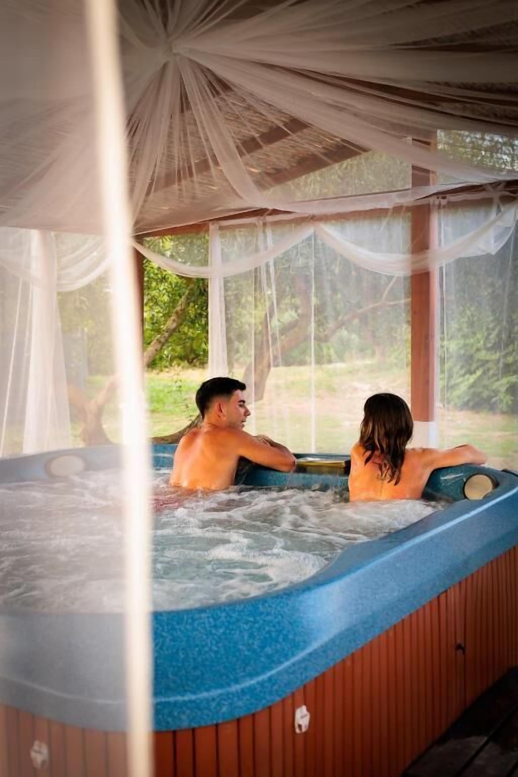 Ein Whirlpool mit Baldachin, umgeben von Holzwänden und Blick auf Grün.