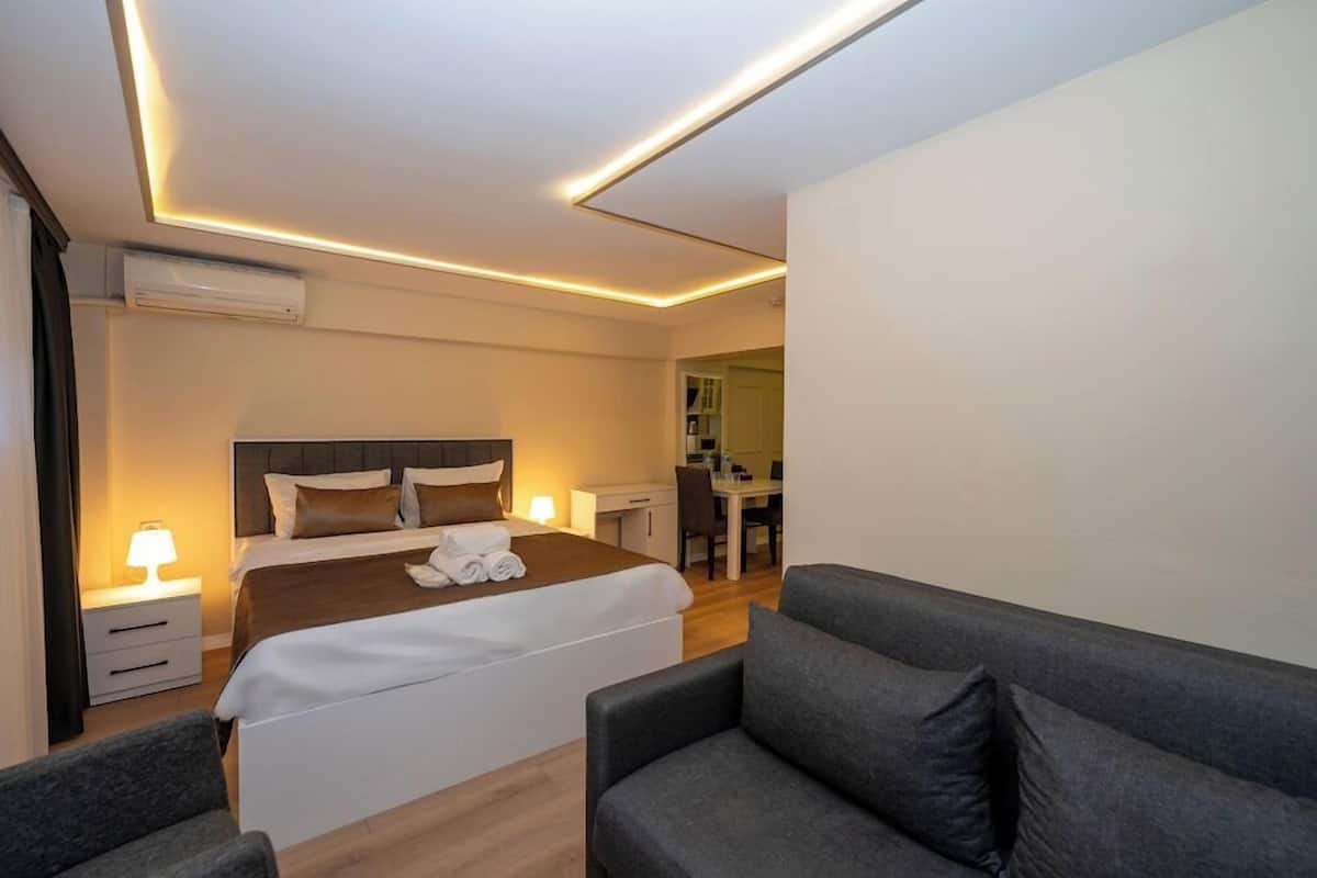 A modern hotel room with a neatly made bed, a sofa, a desk, and a chair.