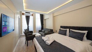 Habitación de hotel con una cama grande, un sofá, un televisor y un televisor de pantalla plana montado en la pared.