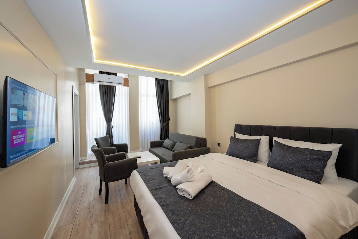 A hotel room with a large bed, a sofa, a TV, and a flat-screen TV mounted on the wall.