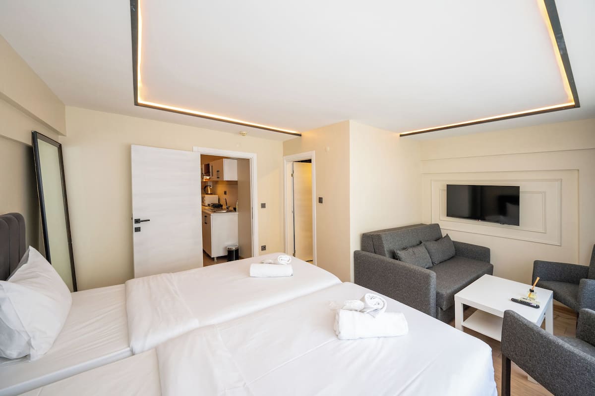 A hotel room with two beds, a sofa set, a TV, and a small table.