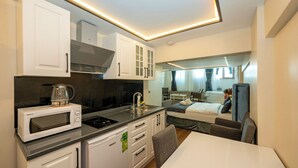Una kitchenette compacta con microondas, estufa y pileta. Se observa en el fondo un pequeño comedor con mesa y sillas.