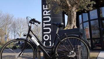 Een zwarte fiets geparkeerd naast een bord waarop 'COUTURE' staat.