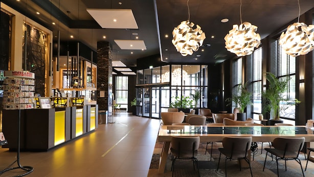 A modern hotel lobby with a reception desk, seating area, and large windows. - XO Hotels Couture (Amsterdam)