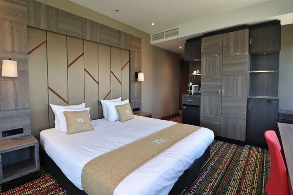 Una habitación de hotel con una cama grande, un escritorio, un armario y una kitchenette.
