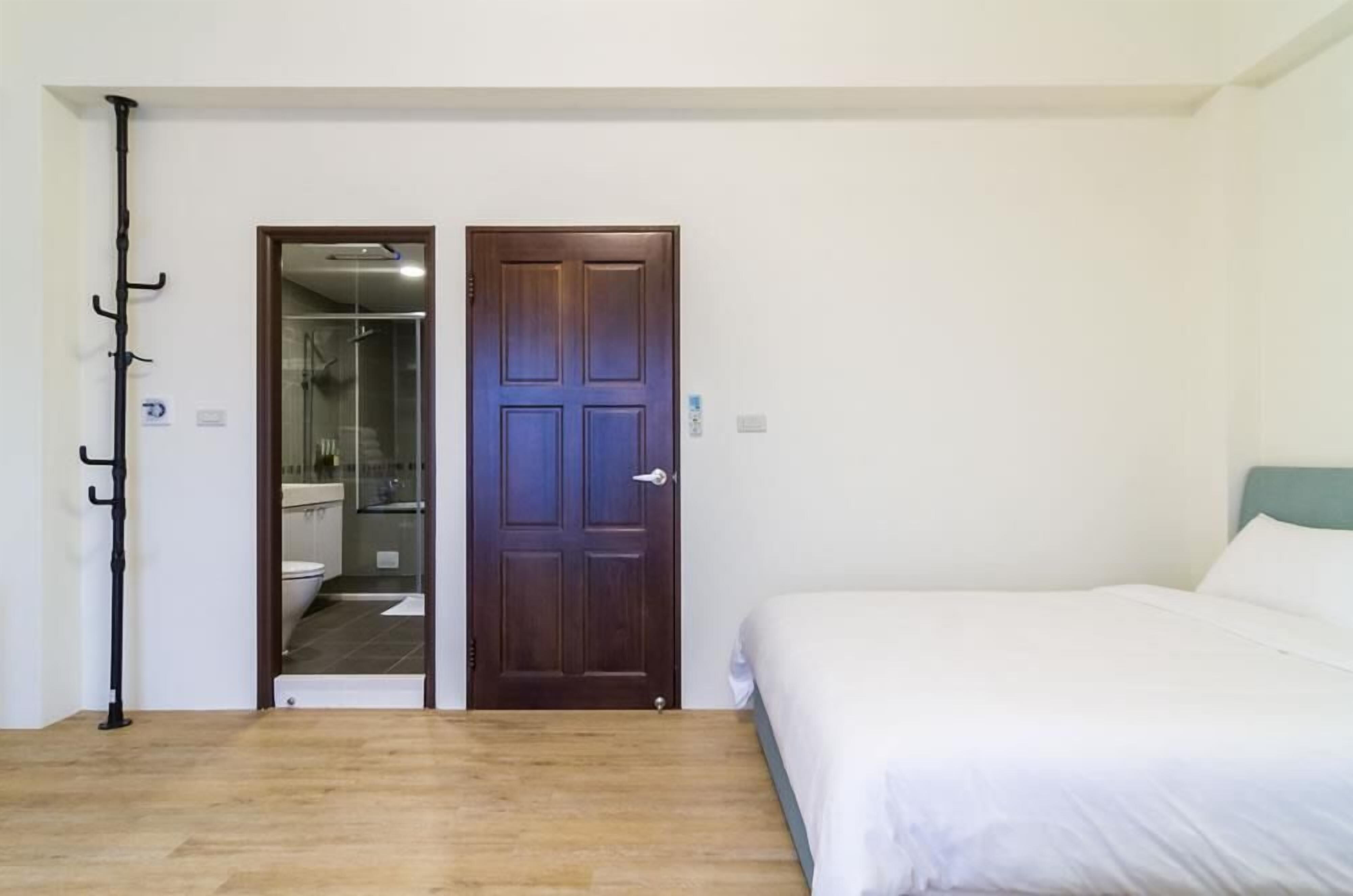Ein Schlafzimmer mit Holzboden, einem weißen Bett und einer Tür zu einem Badezimmer mit Duschkabine.