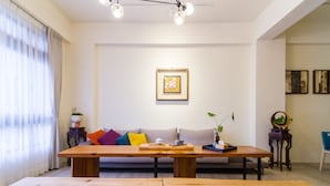 Un salon moderne avec une table à manger en bois, un canapé agrémenté de coussins colorés, une œuvre d’art encadrée au mur et une petite table d’appoint avec une plante.