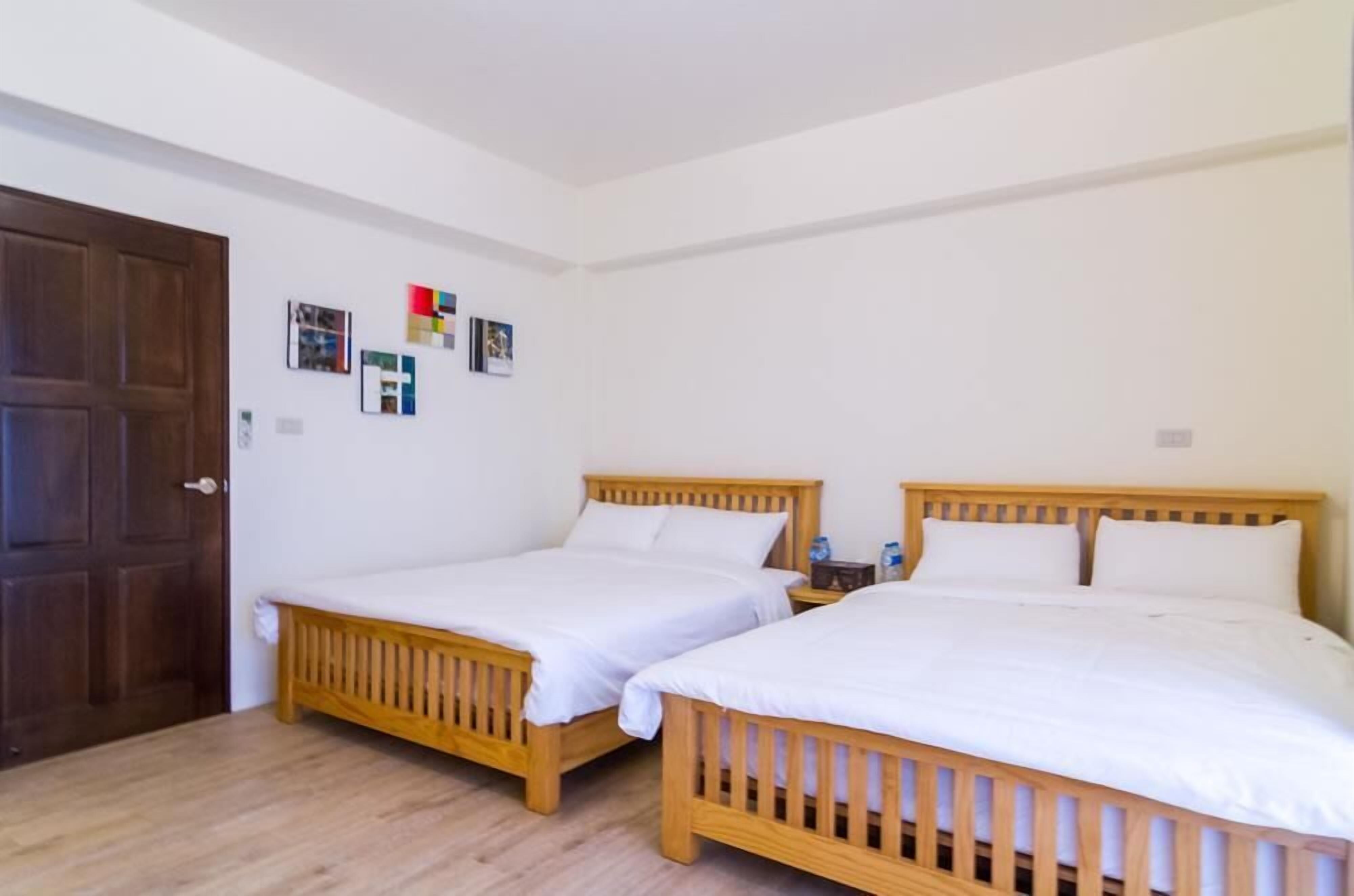 A room with two wooden beds, white bedding, a wooden door, and a wall with framed pictures.