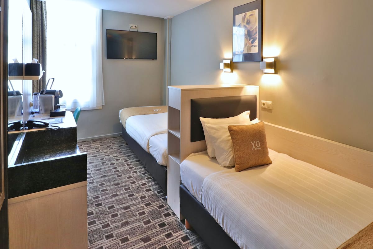 Een hotelkamer met twee bedden, een bureau met een computer, een aan de muur bevestigde televisie en een kamerbreed tapijt met een patroon.