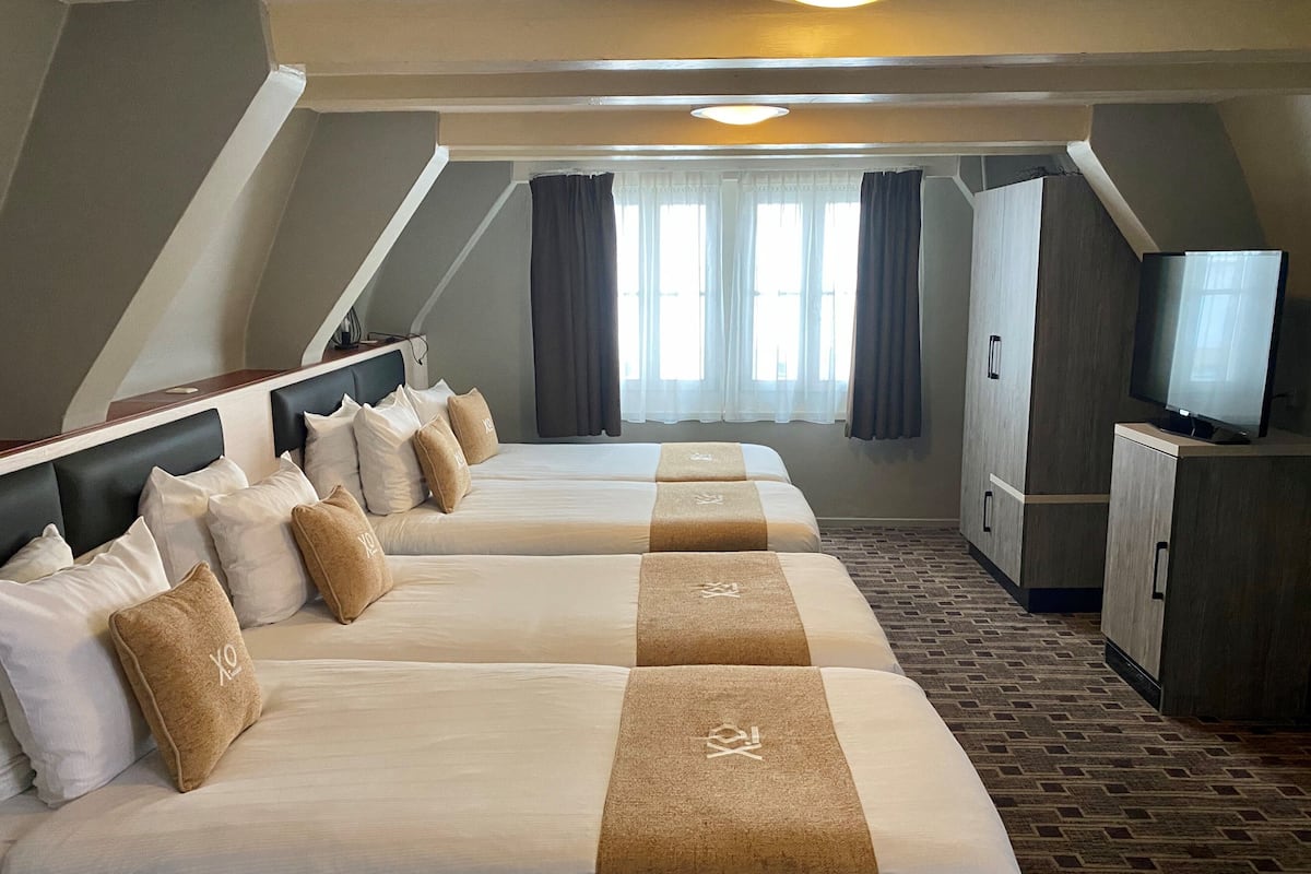 Een hotelkamer met drie bedden, een televisie en een kledingkast.